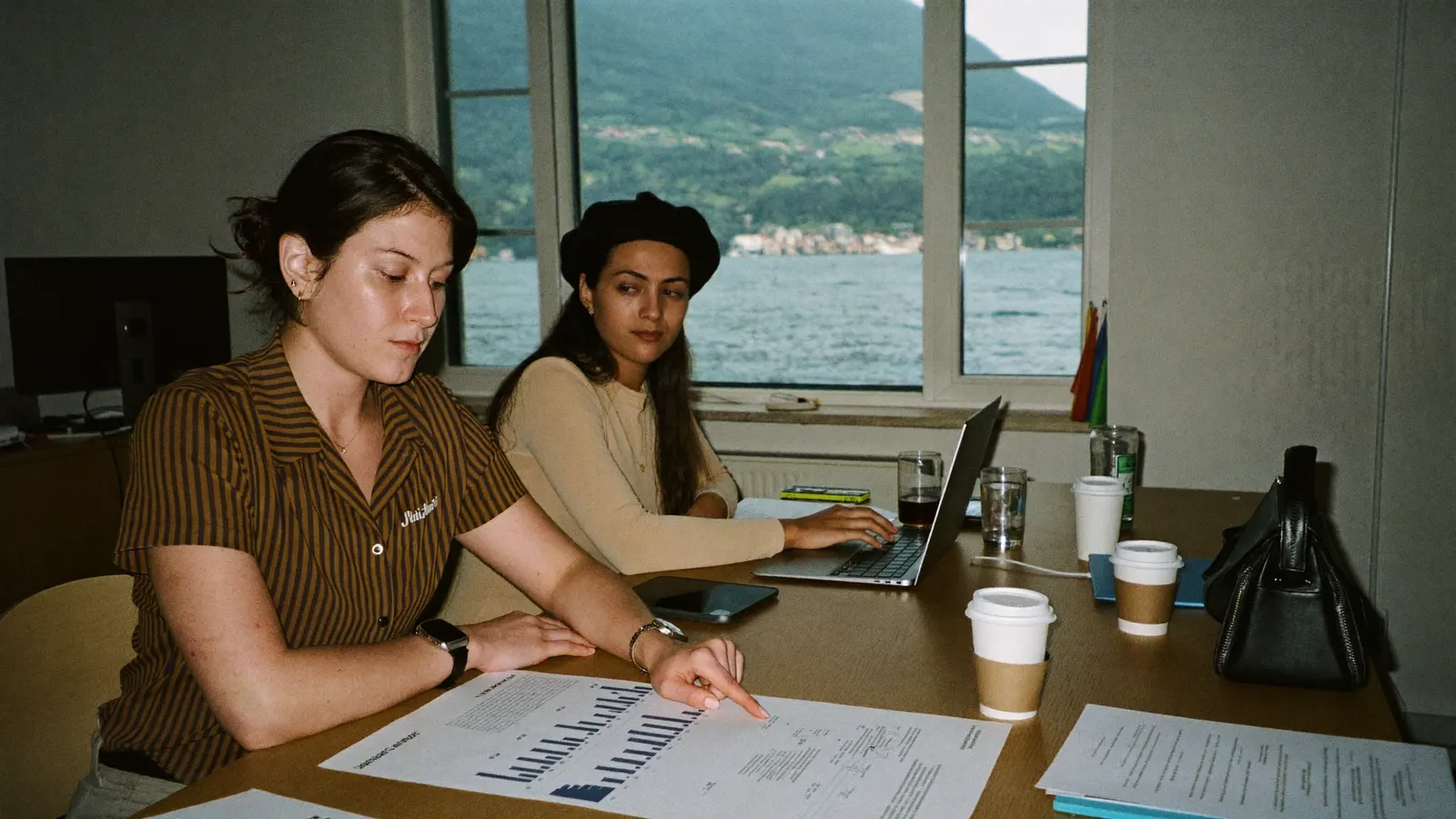 Zwei Frauen besprechen eine Auswertung in einem Büro mit Seeblick